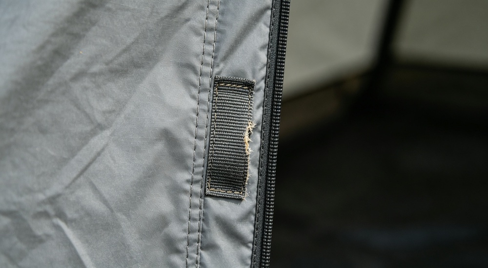 Detail close-up of reinforced door edge on blue relief tent tarpaulin, wear strip and double stitching reinforcement visible showing high-traffic area durability enhancement for long-term emergency shelter use Detail close-up of reinforced door edge on blue relief tent tarpaulin, wear strip and double stitching reinforcement visible showing high-traffic area durability enhancement for long-term emergency shelter use