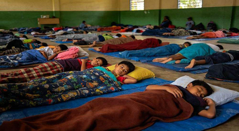 Wide angle view of Southeast Asian school emergency shelter students resting on sleeping bags classroom Wide angle view of Southeast Asian school emergency shelter students resting on sleeping bags classroom
