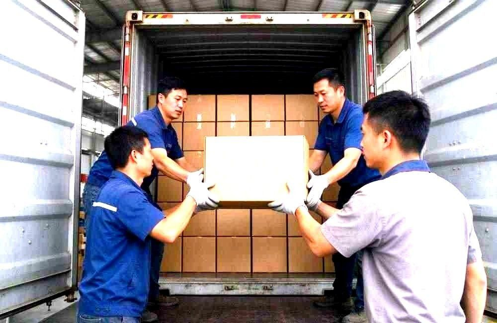 Workers loading mosquito net and bedding cartons into a shipping container for Africa, showing bulk disease prevention supplies export logistics