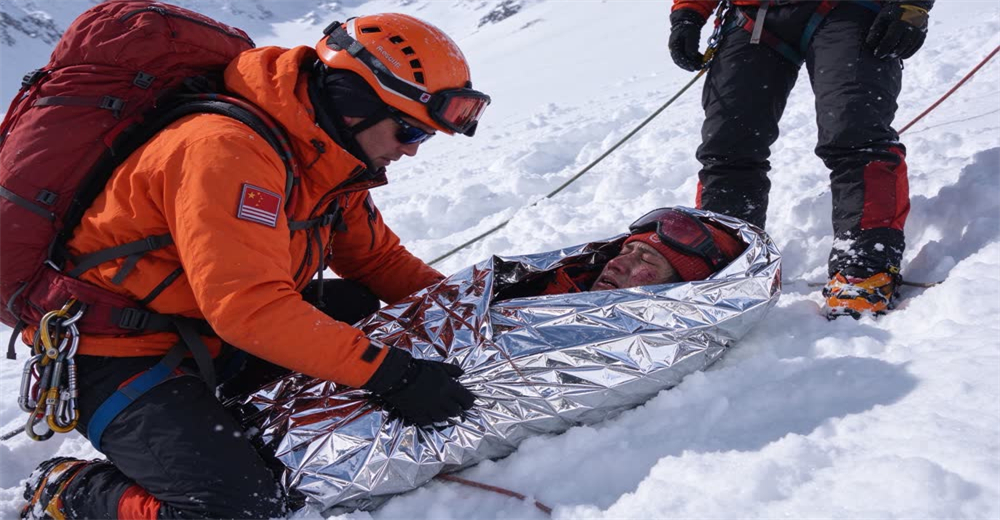 Wide view of avalanche victim wrapped in silver rescue bivvy bag on snow showing thermal protection after extrication